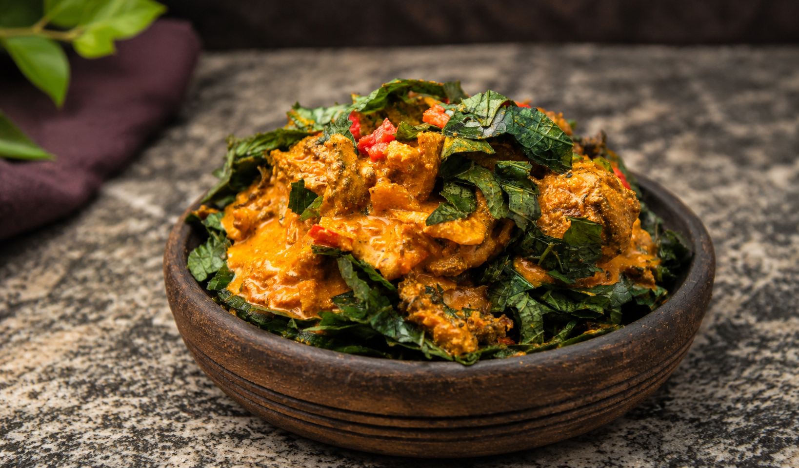 Isi Ewu in a wooden bowl generously topped with sliced utazi leaves
