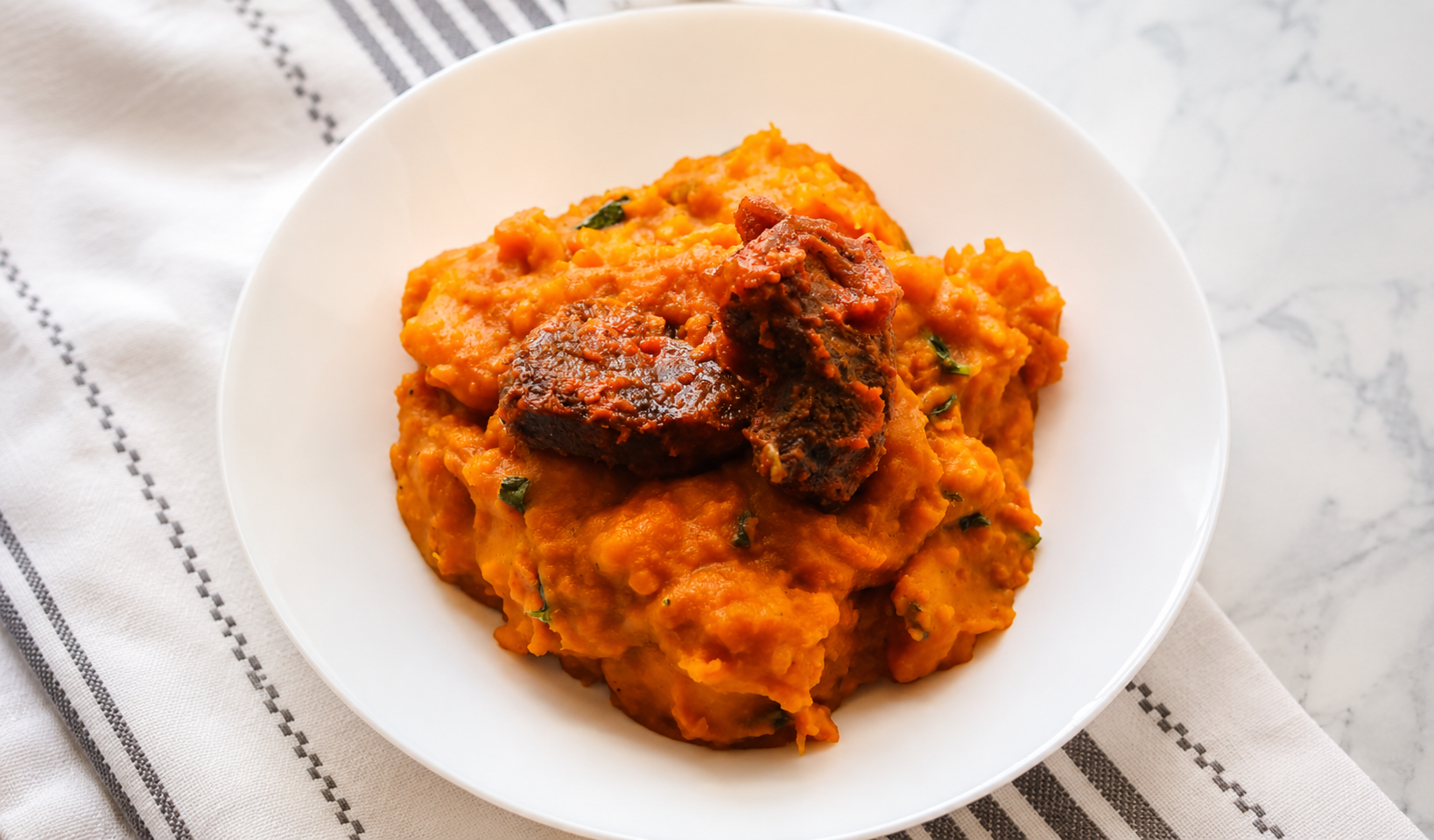 Smooth orange yam pottage with tender beef chunks on a white plate