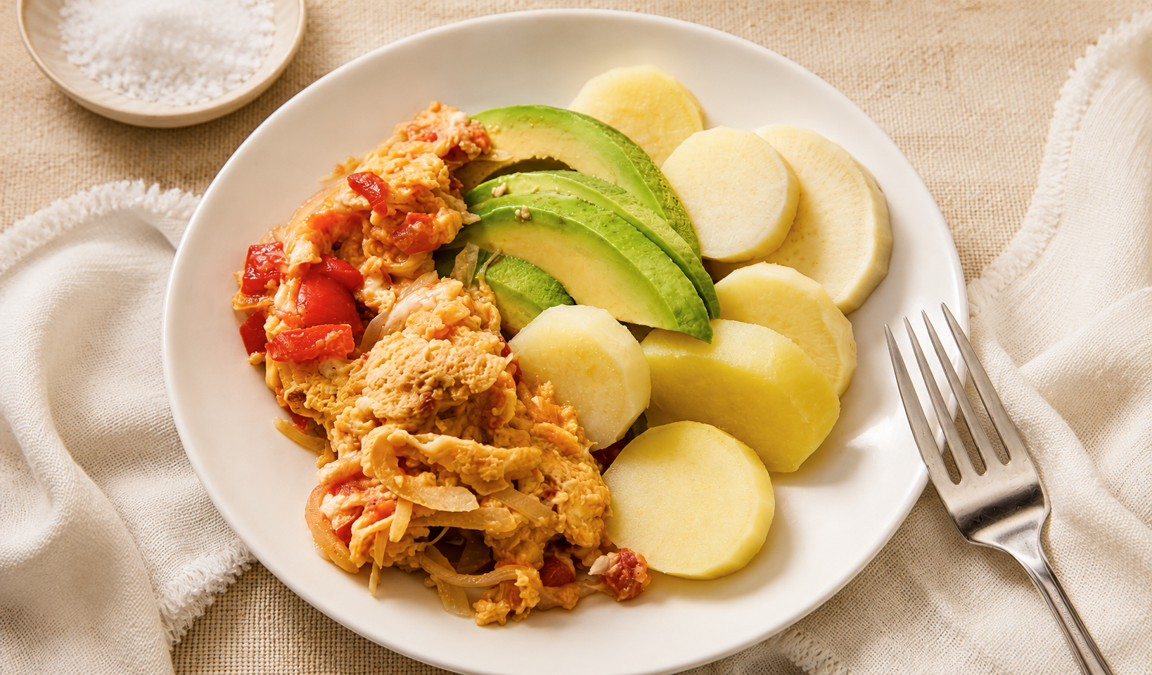 Boiled yam slices with scrambled egg-pepper sauce and avocado on a white plate