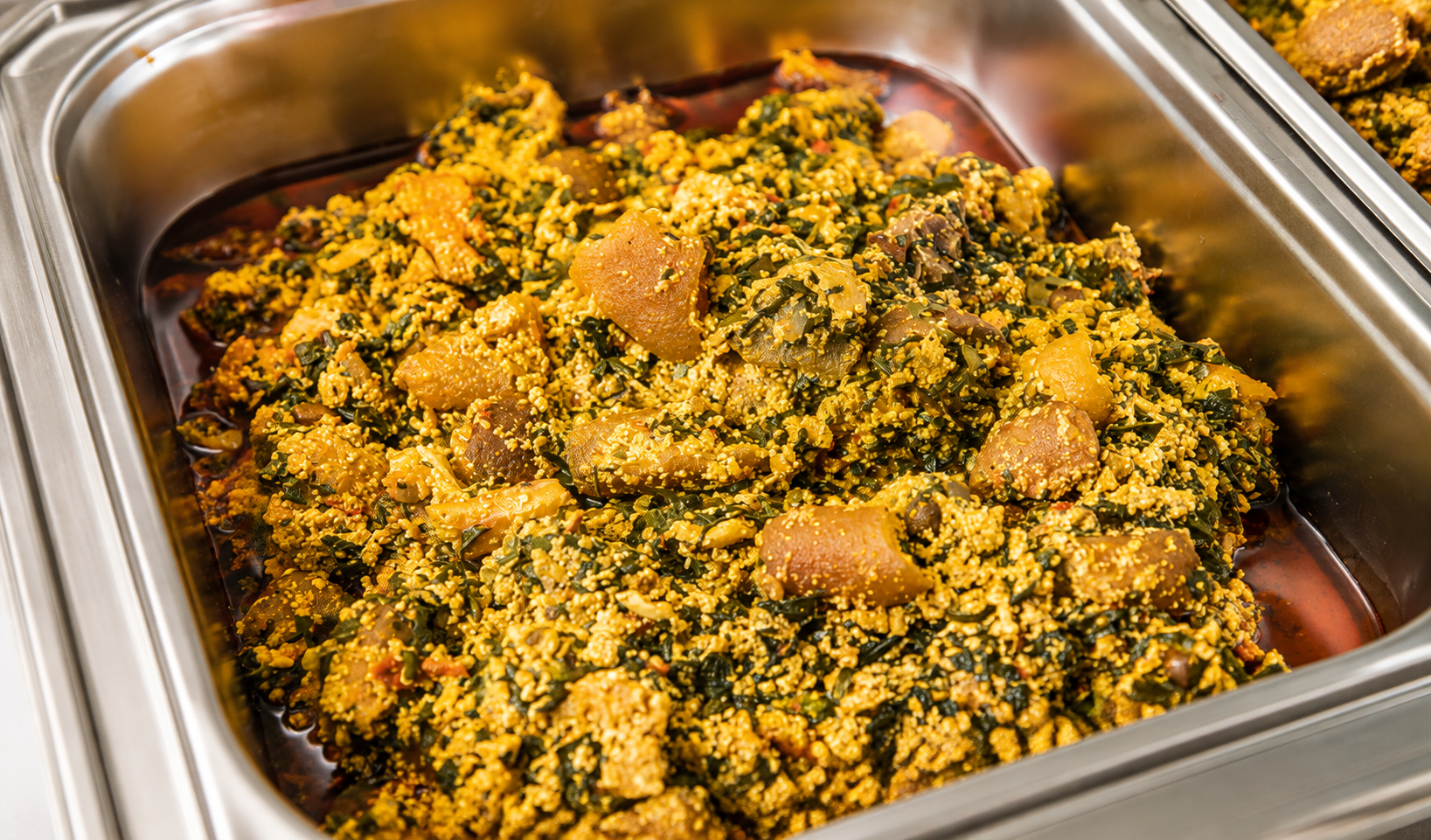 Freshly cooked egusi soup with ugu leaves and meat in a serving tray