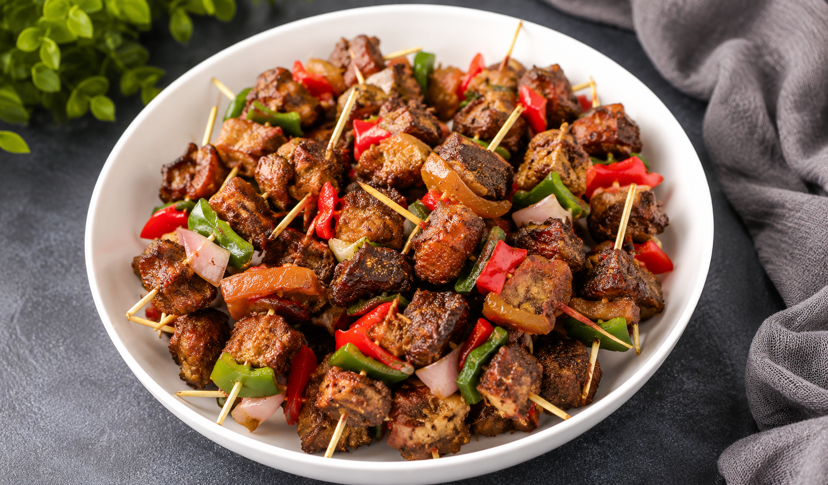 Bowl of suya beef skewers with red and green peppers and onions